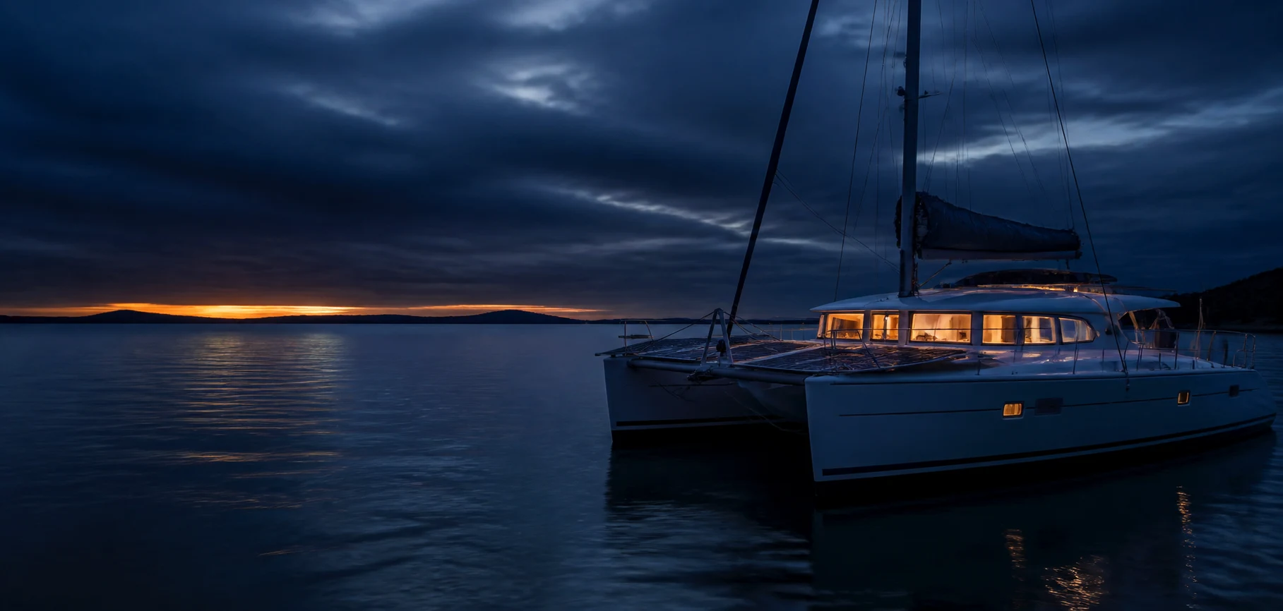 A solar-equipped cruising catamaran at anchor before dawn with weather gathering on the horizon